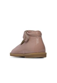 Chaussure à cheville en cuir rose clair avec une finition brillante. Présente un design découpé et une sangle Velcro ajustable. Semelle en caoutchouc pour une bonne adhérence.