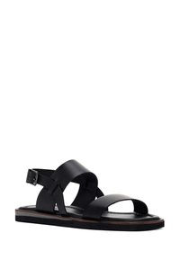 Black leather sandal with wide straps, open toes, and an adjustable ankle buckle. Features a flat sole with a contrasting brown edge.