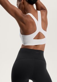 Weißer Sport-BH mit Racerback-Design und Ausschnittdetails, kombiniert mit hoch geschnittenen schwarzen Leggings mit dezentem Branding.