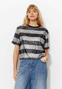 Haut à manches courtes rayé de sequins noirs et argentés, avec un col rond, associé à un pantalon en jean taille haute. Coupe ample.