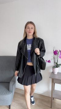 Črna usnjena motoristična jakna, modra skrajšana majica s kratkimi rokavi z belim napisom, črna nabirana krila in mornarsko modri športni čevlji. Notranja postavitev z orhidejami.