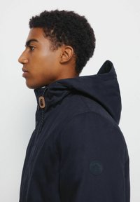 Giacca con cappuccio di colore blu navy, dotata di chiusura con zip e bottoni, realizzata in tessuto testurizzato e con un patch rotondo con logo sulla manica sinistra.