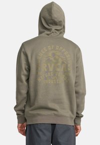 Olijfgroene hoodie met een getextureerde afwerking. Bevat grote gele opdruk op de achterkant met de tekst "RVCA" en decoratieve berggraphics.