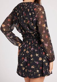 Schwarzes Blumenkleid mit langen, transparenten Ärmeln; geraffte Taille; zeigt eine Mischung aus roten, rosa und gelben Blumen auf einem strukturierten Stoff.