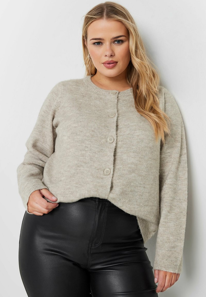 Ljus beige stickad cardigan med rund halsringning och fem knappar framtill. Har långa ärmar och en lätt kortad nederkant.