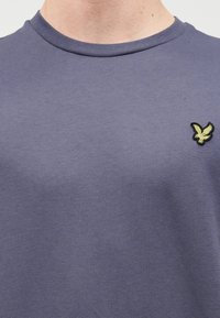 Μπλούζα από βαμβάκι σε ναυτικό μπλε χρώμα με στρογγυλή λαιμόκοψη και κοντά μανίκια. Διαθέτει μικρό κέντημα με κίτρινο και μαύρο λογότυπο αετού στο στήθος.