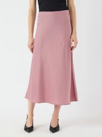 Une longue jupe rose fluide en tissu lisse, avec un design simple et un ourlet droit. Associée à des escarpins noirs à bout pointu.