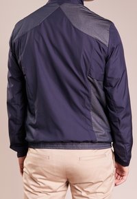 Marinblå vindjacka med en slimmad design, texturerade meshpaneler och resårmidja för en åtsittande look.