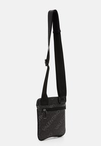 Kompakt svart axelremsväska med justerbar axelrem, framficka med dragkedja och Valentino-logomönster över ytan.