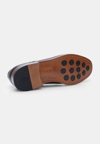 Suola in pelle con una finitura texture marrone, dotata di un tacco nero e di numerosi grip circolari in gomma sul fondo per una maggiore aderenza.