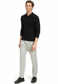 Schwarzes Langarm-Polohemd mit Kragen und Knopfleiste, kombiniert mit hellgrauen Jogginghosen und schwarzen Turnschuhen. Glatte Stofftextur.