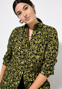 Camisa de botones con estampado de leopardo verde y negro, con cuello, mangas largas y una textura suave con acentos amarillos.