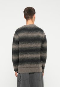 Knitted sweater in black and beige stripes, featuring a round neck and ribbed hem. Soft texture with a relaxed fit.
