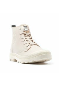 Sneaker alto color off-white con suola spessa e texturizzata, chiusura con lacci, patch con logo sulla linguetta e linguetta sul tallone, su sfondo bianco.