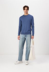 Blue crew-neck sweater in a soft knit, paired with light blue straight-leg jeans and white sneakers, holding a beige canvas tote bag.