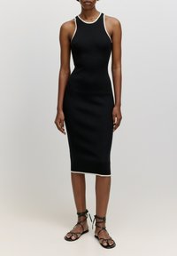 Schwarzes geripptes Midi-Kleid mit weißen Akzenten, figurschmeichelnde Silhouette, ärmelloses Design. Getragen mit schwarzen Riemchensandalen, die den Knöchel betonen.