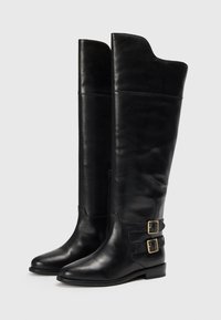 Botas negras de piel hasta la rodilla con una textura suave, punta redonda, tacón bajo y dos hebillas decorativas a los lados.