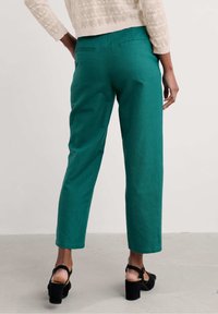 Zielone, dopasowane spodnie z prostą nogawką i subtelną teksturą. Posiadają dwie kieszenie z tyłu i są noszone z czarnymi obcasami.