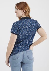 Polo-shirt imprimé floral bleu marine avec des manches courtes, col et poignets noirs contrastés, et ourlet arrondi. Tissu en coton léger.