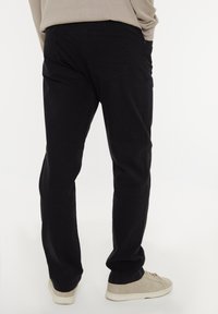 Pantaloni neri in cotone con un design a gamba dritta, dotati di due tasche posteriori e una texture liscia. Indossati con sneakers di colore chiaro.