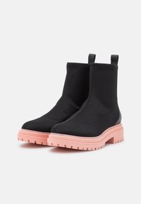 Botines negros hechos de tela con una suela de goma rosa, con una textura suave y cómodos tiradores para ponérselos fácilmente.