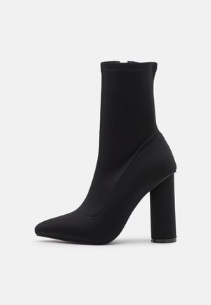 Sort ankelstøvle lavet af glat stof, med spids tå og en kraftig høj hæl. Sømløst design med elastisk side for nem påtagning.