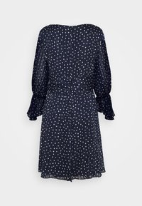 Robe bleu marine à pois avec manches longues transparentes, taille froncée et poignets évasés. Tissu léger à texture froissée et coupe fluide.