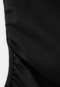 Crni teksturirani materijal s nabranim elastičnim detaljem duž zakrivljenog ruba, vjerojatno dio odjevnog predmeta.