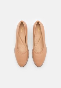 Ballerines en cuir beige avec bout arrondi, bords élastiqués et semelle intérieure perforée pour la respirabilité. Texture lisse avec un minimum de détails métalliques.