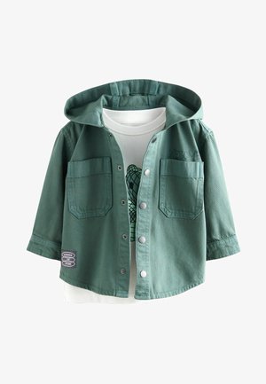 Zeleno usnjeno jakno s kapuco, zapiranjem na gumb, dvema žepoma na prsih in nalepko "NAREDITE TO ZABAVNO"; prek bele grafične majice.