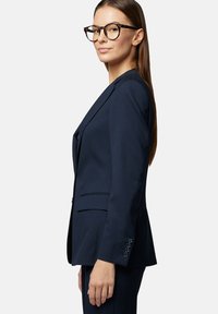 Granatowa marynarka o dopasowanym kroju, z pojedynczym guzikem i klapami typu notch. Posiada mankiety z czterema guzikami oraz subtelnie teksturowany materiał.