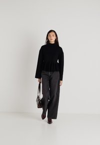 Svart langermet topp med høy hals, peplum-bunn, parret med høy midje, vid-beinte svarte jeans og burgunder hælhæler. Holder en brun veske.