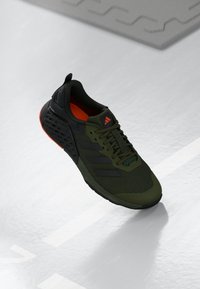 Baskets de sport vert olive avec accents noirs, dessus en maille et doublure intérieure orange. Présente trois rayures noires et une semelle texturée.