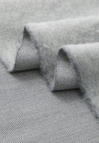 Grå uldstof med en blød, fluffy tekstur lagd over en tynd, grå stribet tekstil, der viser kontrasterende materialer og design.