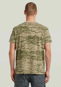 Camo-patroon kortemouwen t-shirt in aardse groentinten; gestructureerde stof met een subtiele raster; het ontwerp op de achterkant heeft ongelijkmatige streepjespatronen.