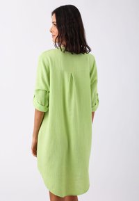 Robe chemise texturée vert clair, avec une coupe ample, des manches retroussables et un pli au dos pour plus de détails. Surface du tissu lisse.