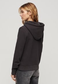 Felpa grigia scura con una texture morbida, dotata di un grande cappuccio, polsini a coste e una vestibilità rilassata, abbinata a jeans neri sbiaditi.