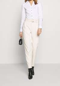 Vit figursydd skjorta med knappr detaljer, kombinerad med högmidjade krämfärgade byxor som har ett bälte. Svarta texturerade ankboots och en liten handväska.