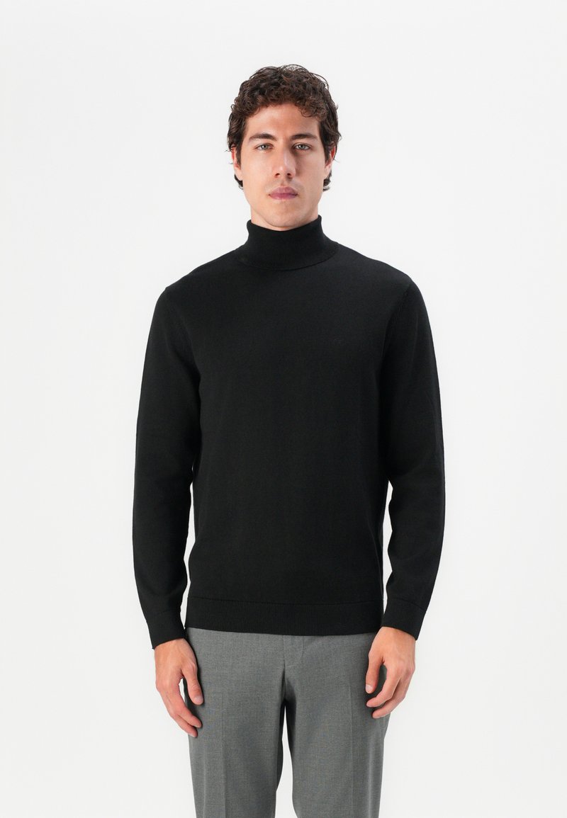Schwarzer Rollkragenpullover aus weichem Strickmaterial, mit taillierter Passform und langen Ärmeln, kombiniert mit grauen Hosen.