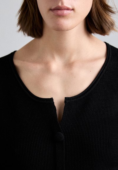 Black ribbed knit sweater featuring a round neckline and a single button closure at the front, detail on the collar edge visible.