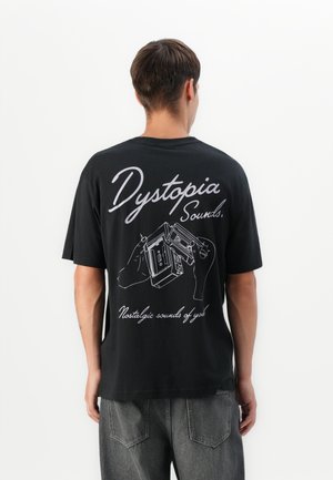 Man wearing black t-shirt with white graphic of hands holding cassette tapes and text "Dystopia Sounds. Nostalgic sounds of youth."