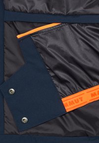 Navy insulated jacket interior featuring a smooth fabric, orange zipper, and a contrasting brand label. Silver snap closures present.