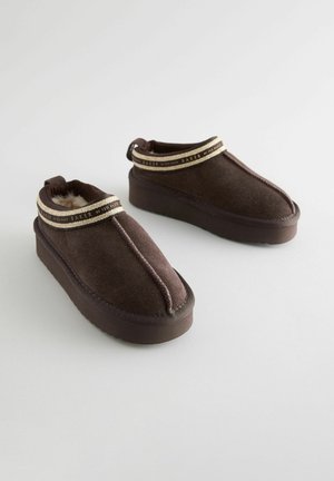 Hnedé semišové členkové čižmy s hrubou platformou, ktoré majú kontrastný béžový pás okolo vrchu a pútko na zadnej strane.