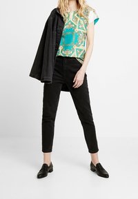 Top de manga corta con estampado en turquesa y dorado, combinado con jeans ajustados negros y una chaqueta de mezclilla negra, completado con mocasines negros.