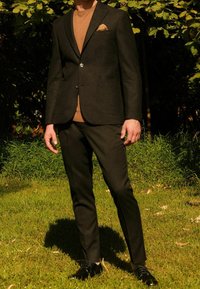 Ciemny garnitur o dopasowanym kroju, zestawiony z brązowym swetrem. Charakteryzuje się fakturowaną tkaniną, srebrnymi guzikami oraz poszetką. Czarne buty.