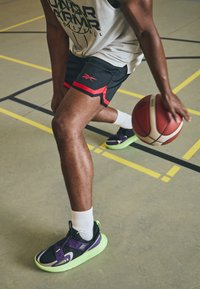 Must have musto püksid musta värviga punaste detailidega, ühendatud lillade ja roheliste tossudega. Näitavad tekstuurset kangast ja sportlikku disaini.
