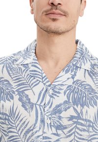 Camisa de manga corta de tejido blanco con un patrón de hojas tropicales en azul. Las características notables incluyen un cuello de campamento y cierre frontal de botones.