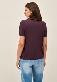 T-paita lyhyillä hihoilla ja pyöreällä kaula-aukolla tumman violetista kankaasta, yhdistettyinä vaaleansinisiin farkkuihin, jotka näyttävät rentoa istuvuuttaja pehmeää tekstuuria.