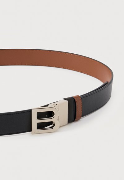 Μαύρη και καφέ δερμάτινη ζώνη με μεγάλο ασημένιο αγκράφα σε σχήμα γράμματος Β, απλωμένη επίπεδα σε λευκό φόντο.