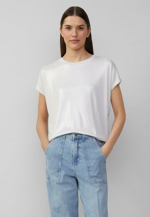 T-shirt blanc à manches courtes avec une texture légèrement brillante, col rond et coupe décontractée, associé à un jean en denim bleu clair taille haute.